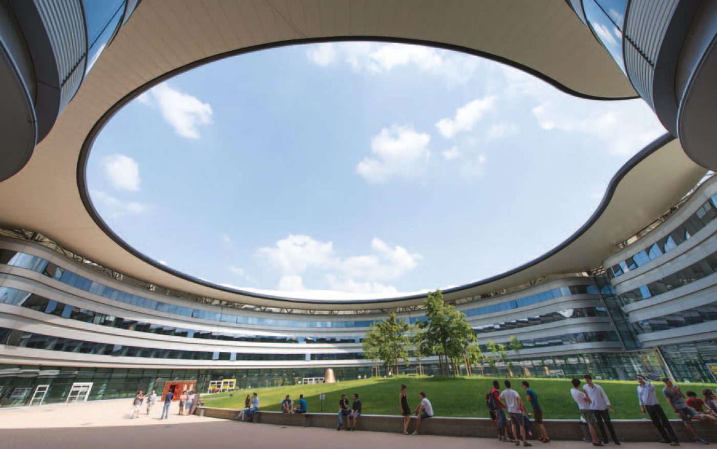 Cortile interno del Campus Luigi Einaudi, circondato da edifici curvi e coperto da un’ampia apertura ovale sul cielo, con prato centrale e gruppi di studenti.