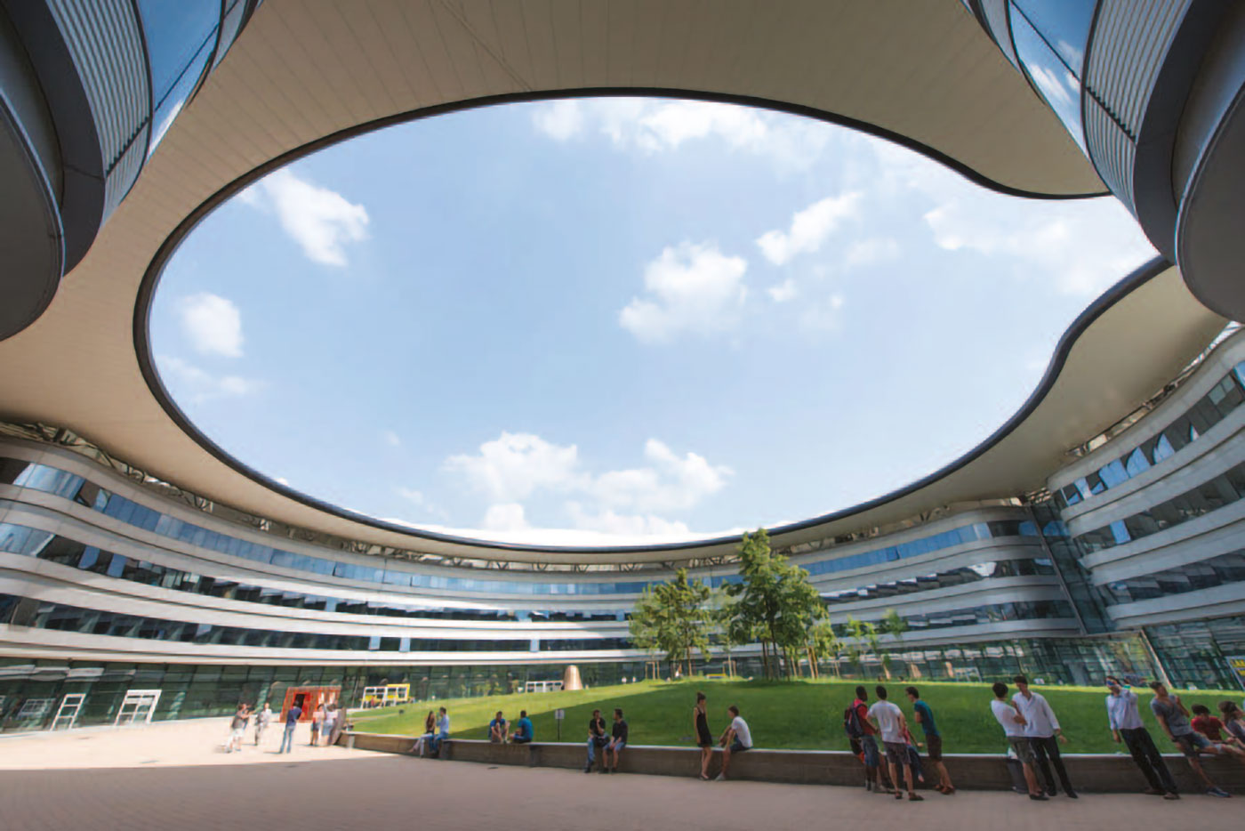 Cortile interno del Campus Luigi Einaudi, circondato da edifici curvi e coperto da un’ampia apertura ovale sul cielo, con prato centrale e gruppi di studenti.