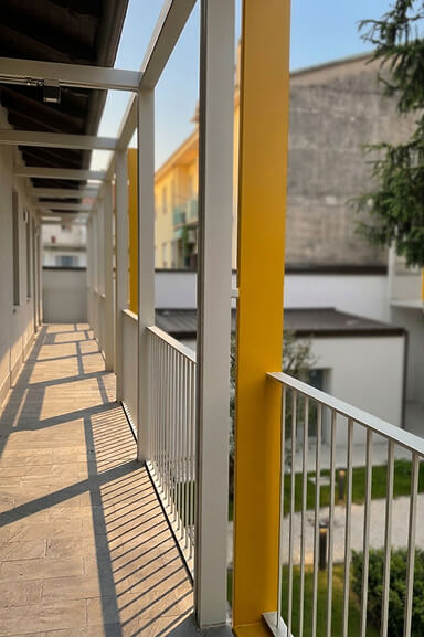 Vista del ballatoio del complesso residenziale, con struttura bianca, pilastri gialli e affaccio sulla corte interna