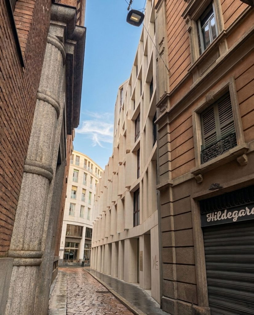Scorcio di una stretta via pavimentata in pietra con un moderno edificio dalla facciata geometrica in pietra chiara integrato tra palazzi storici.