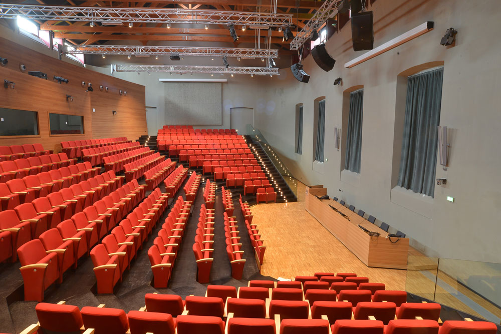 Aula magna con poltrone rosse e palco.