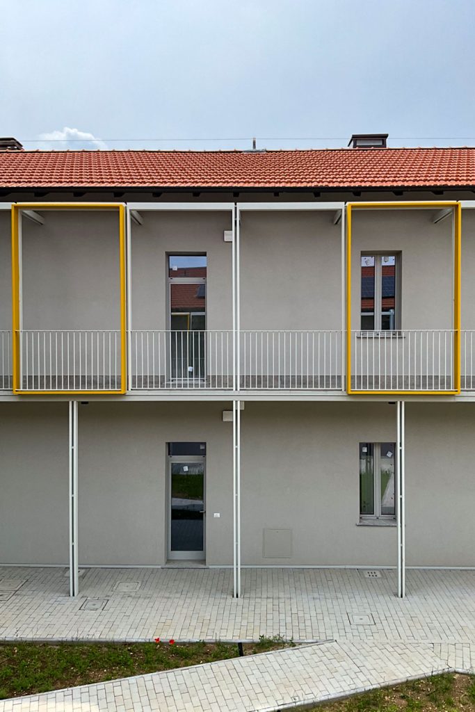 Facciata del complesso residenziale con ballatoio, ringhiere bianche e grandi cornici gialle poste davanti agli ingressi.