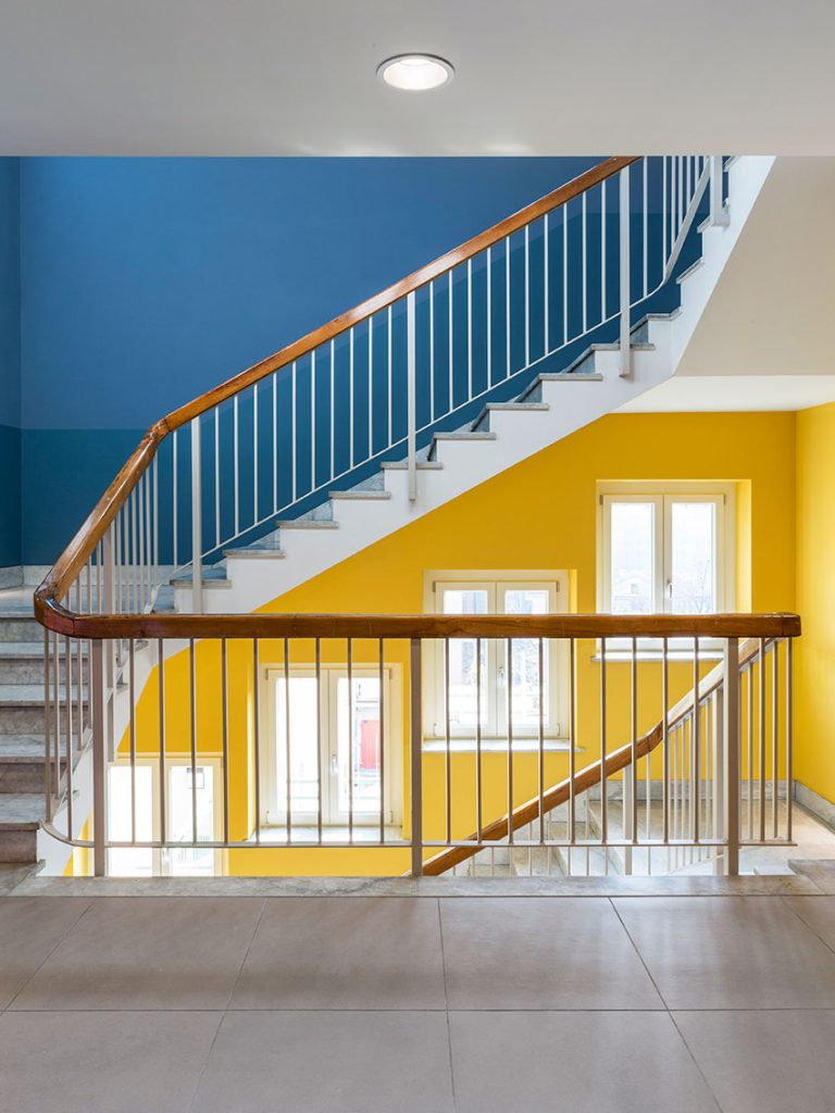 Una persona sale una scala a chiocciola in un moderno edificio con pareti colorate di giallo e verde e finestre.